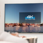 A woman looking at a TV that says "4K Ultra HD" on a background of water and boats.