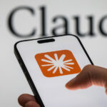 Hand holding iPhone showing Claude logo set against background featuring the Claude logo and text.
