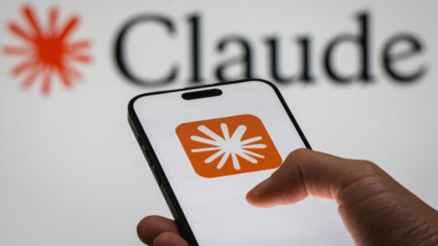 Hand holding iPhone showing Claude logo set against background featuring the Claude logo and text.