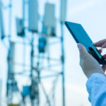 Hands interacting with a smartphone, with a cellular tower in the background.